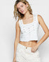Woman wearing a white sleeveless top with button details on a plain background