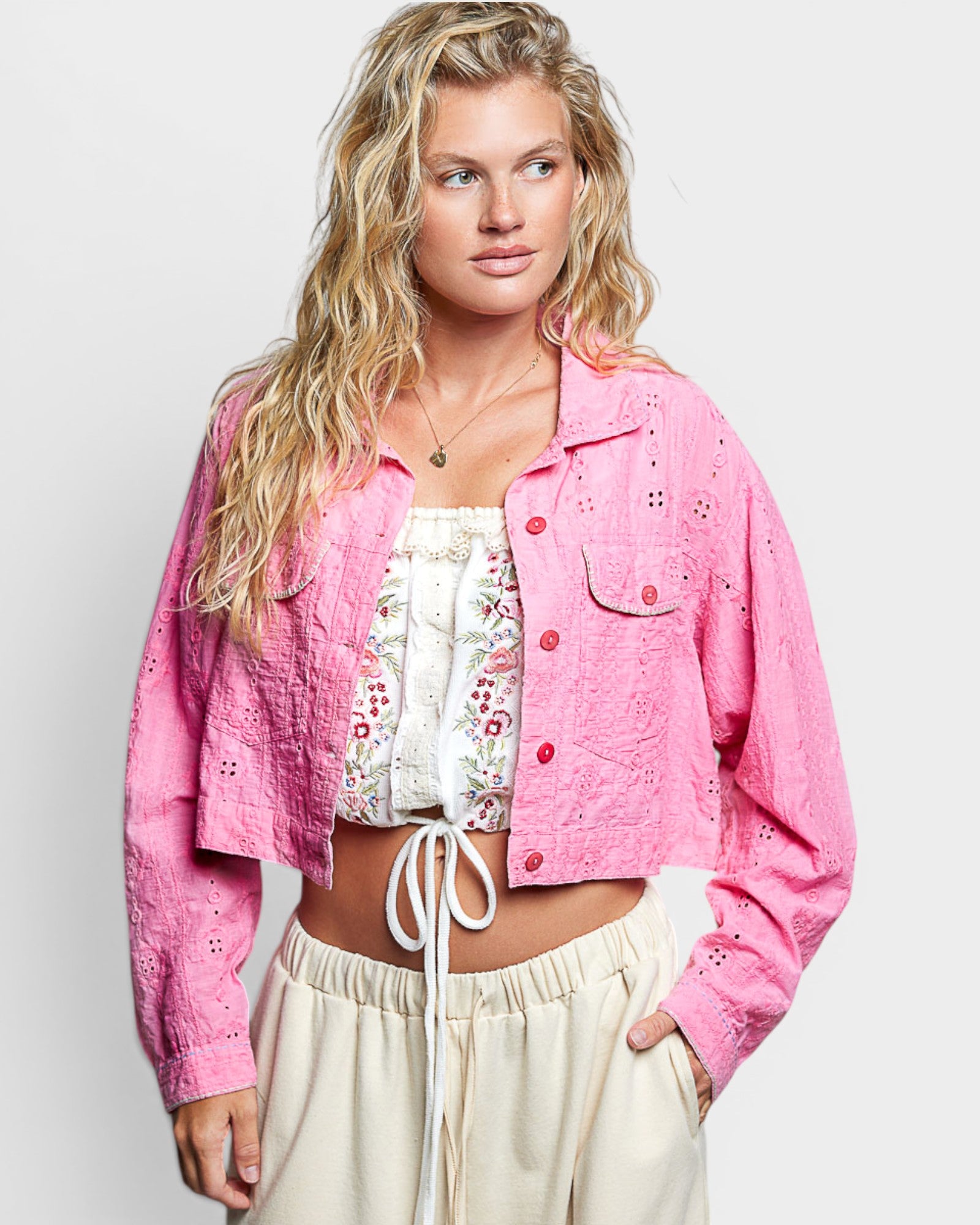 Woman wearing a pink jacket over a floral top and beige pants on a white background