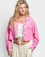 Woman wearing a pink jacket over a floral top and beige pants on a white background
