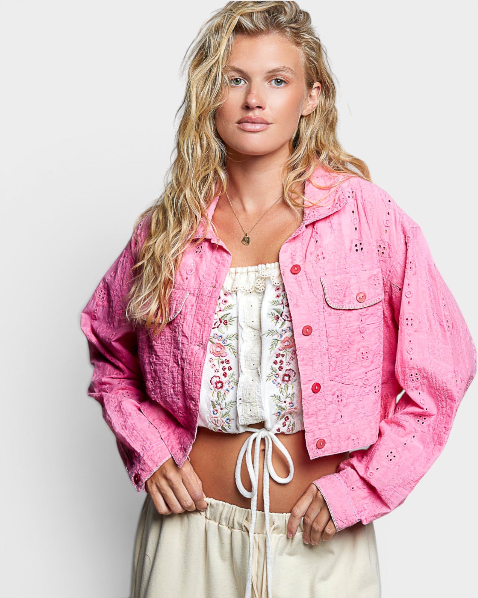 Woman wearing a pink jacket over a floral top and beige pants on a white background