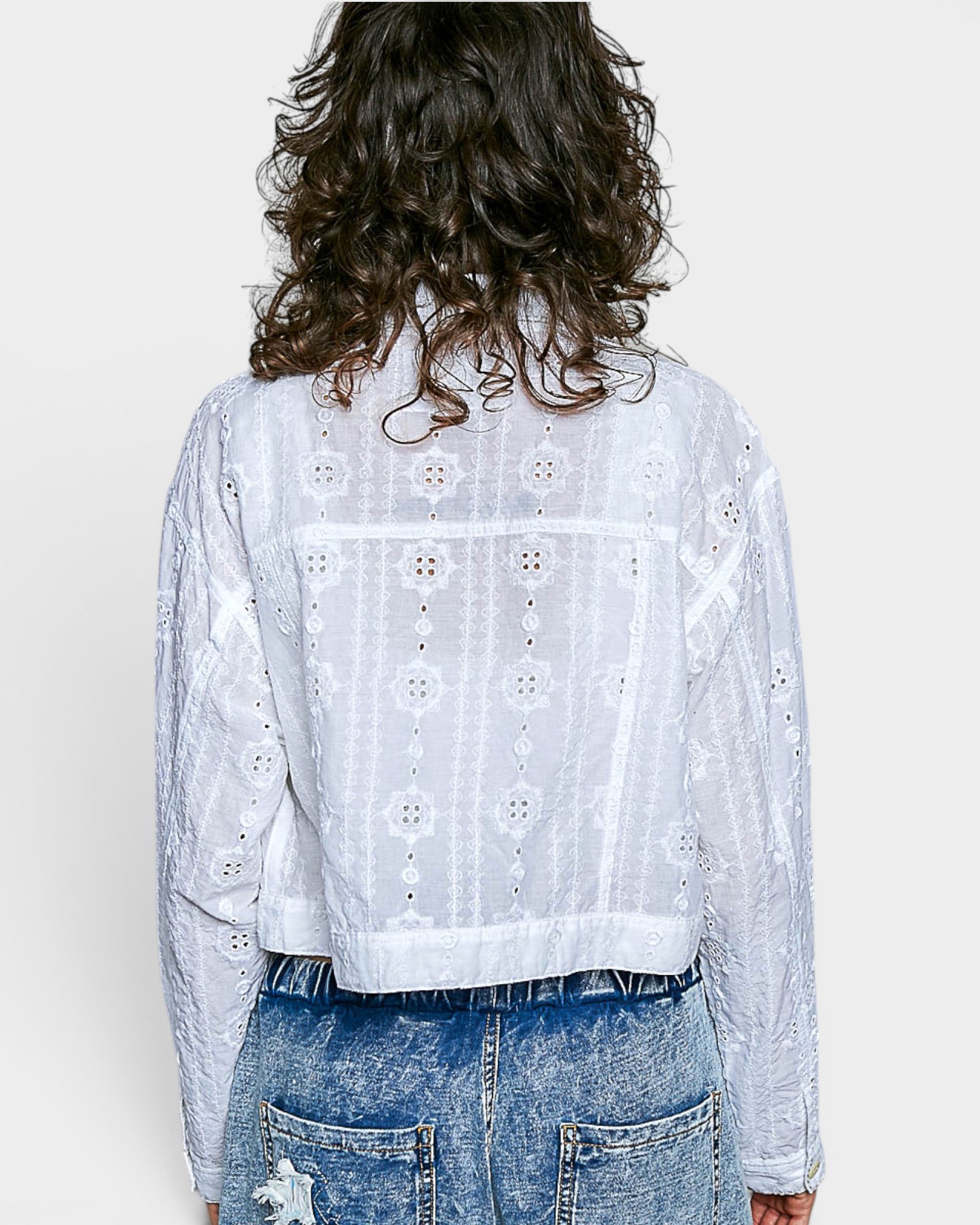Person wearing a white embroidered jacket and blue jeans on a plain background