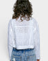 Person wearing a white embroidered jacket and blue jeans on a plain background
