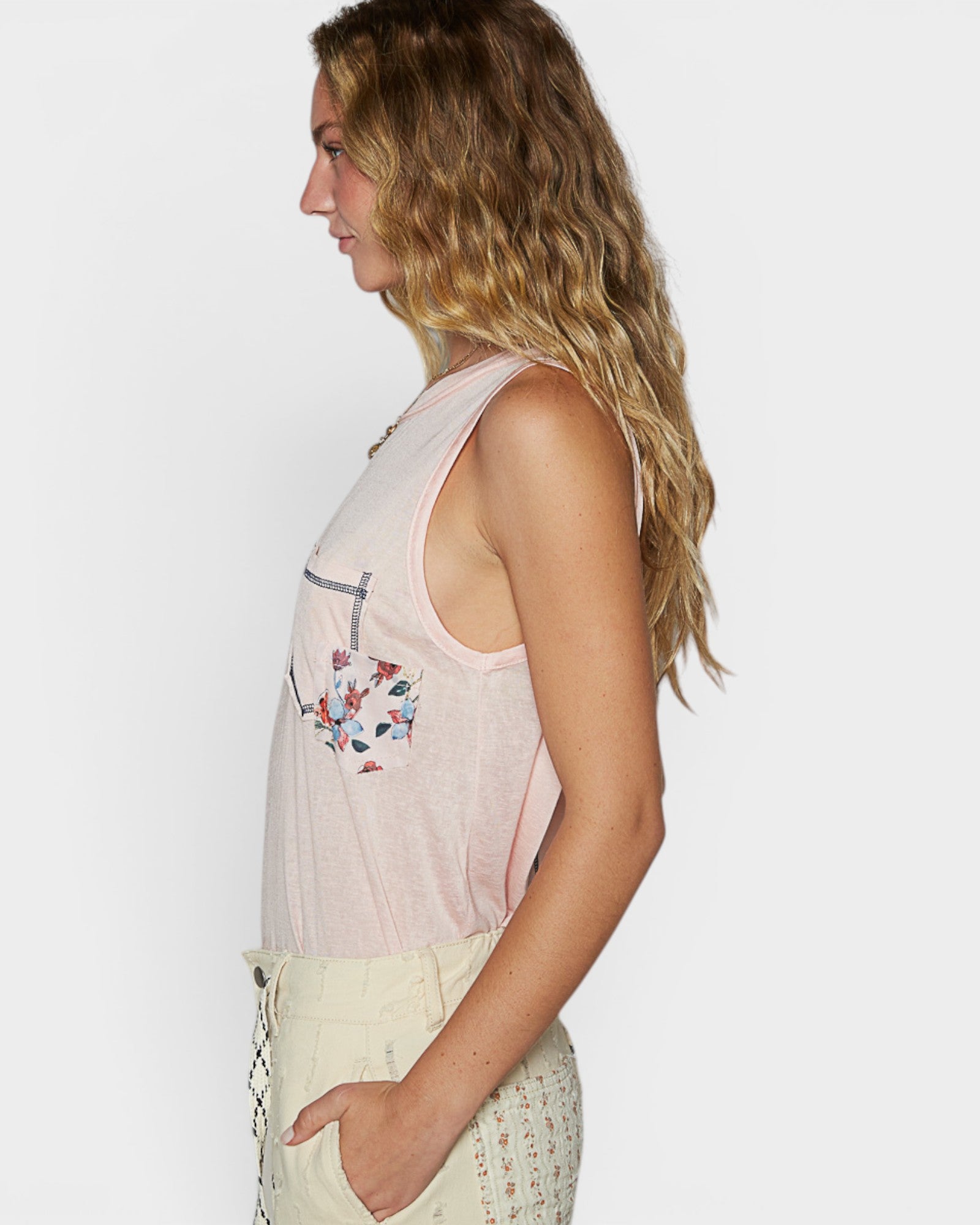 Woman wearing a light pink sleeveless top with floral designs on a plain background