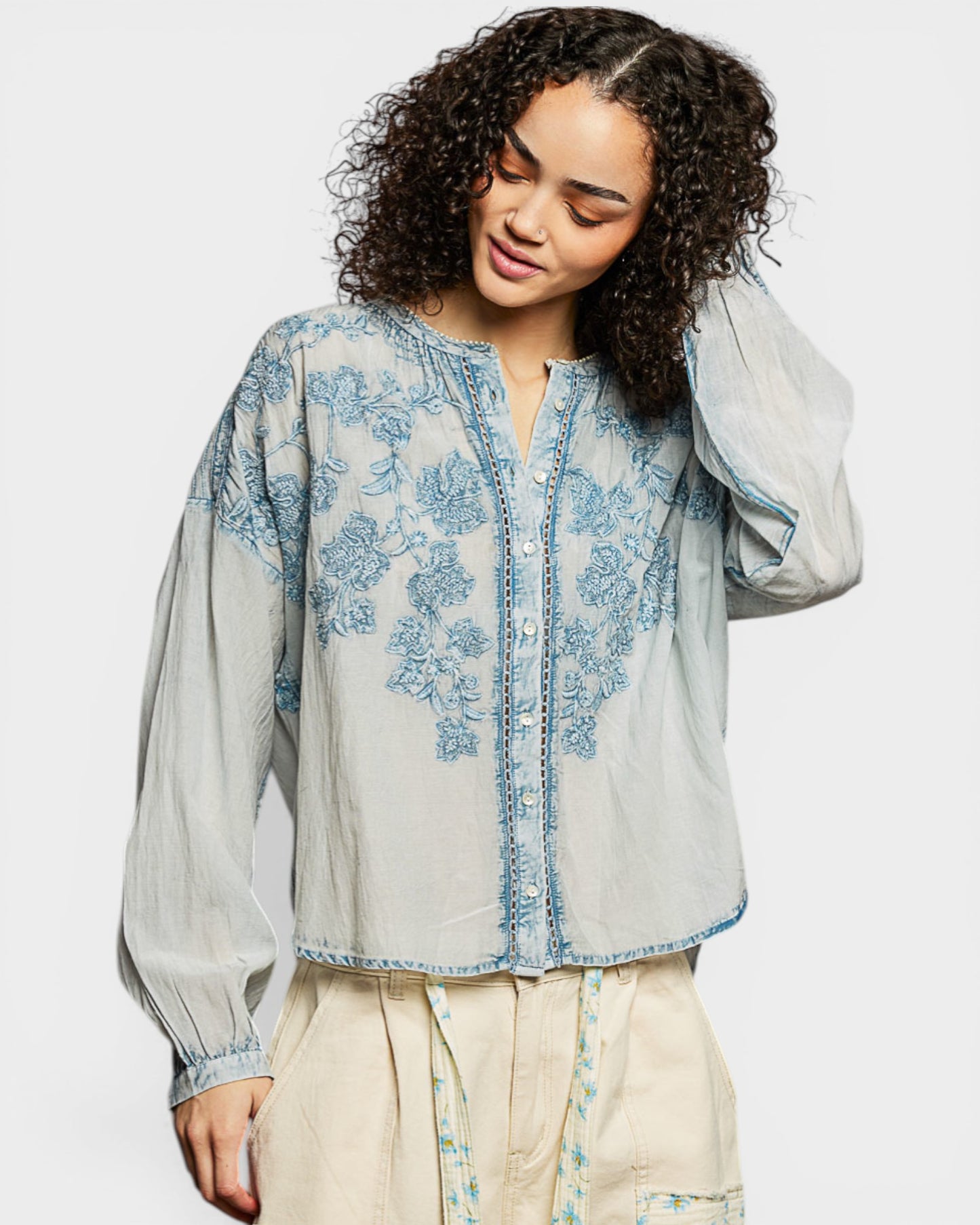 Woman wearing a light blue embroidered blouse with a plain background