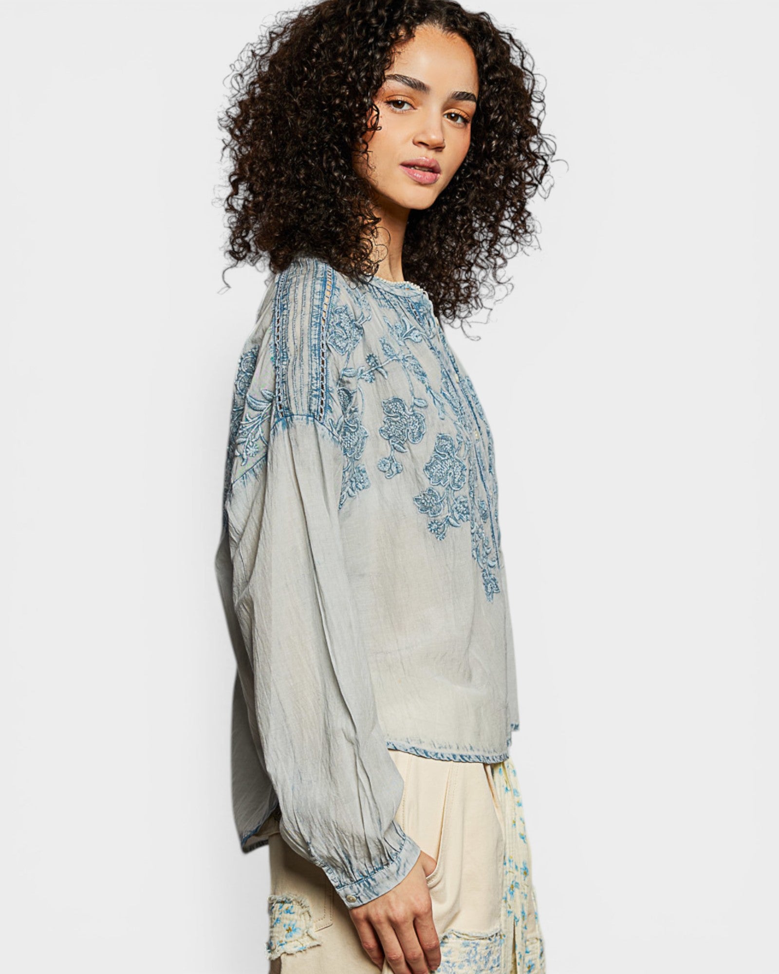 Woman wearing a light blue embroidered top with a plain background