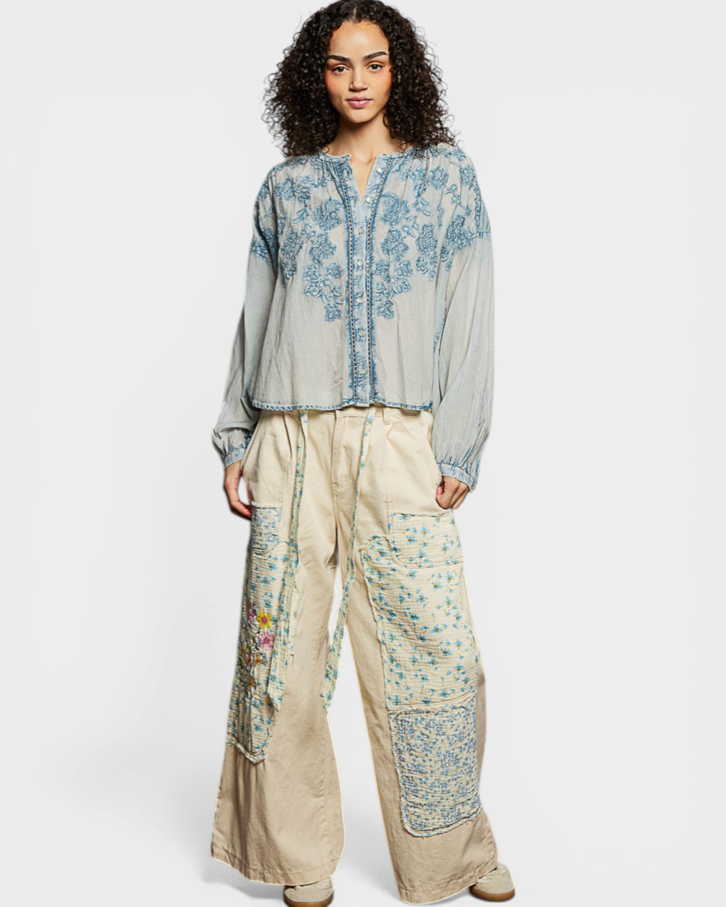 Woman wearing a light blue embroidered top and beige pants on a white background