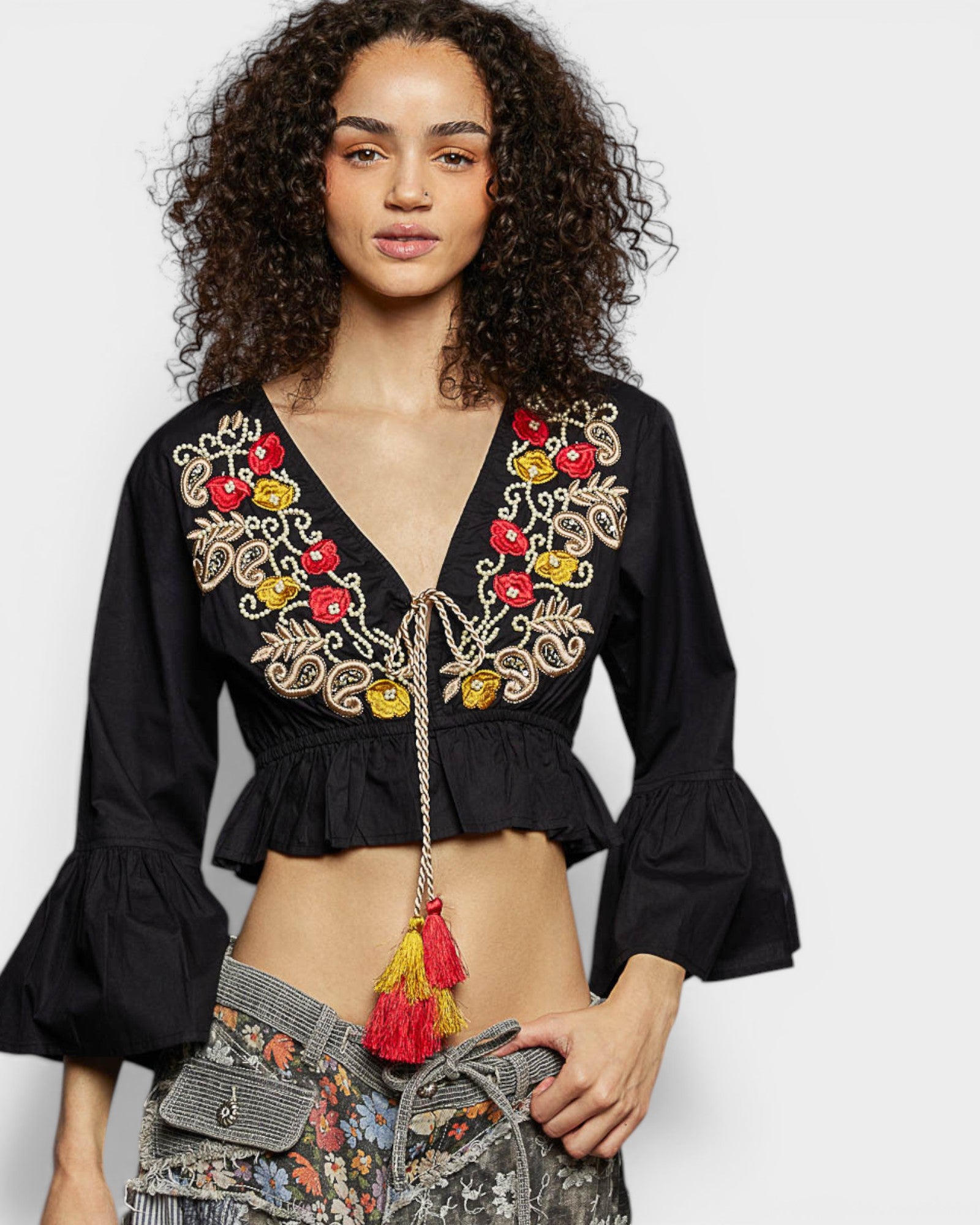 Woman wearing a black embroidered top with colorful details on a white background