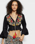 Woman wearing a black embroidered top with colorful details on a white background