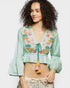 Woman wearing a light green embroidered blouse with colorful designs on a white background