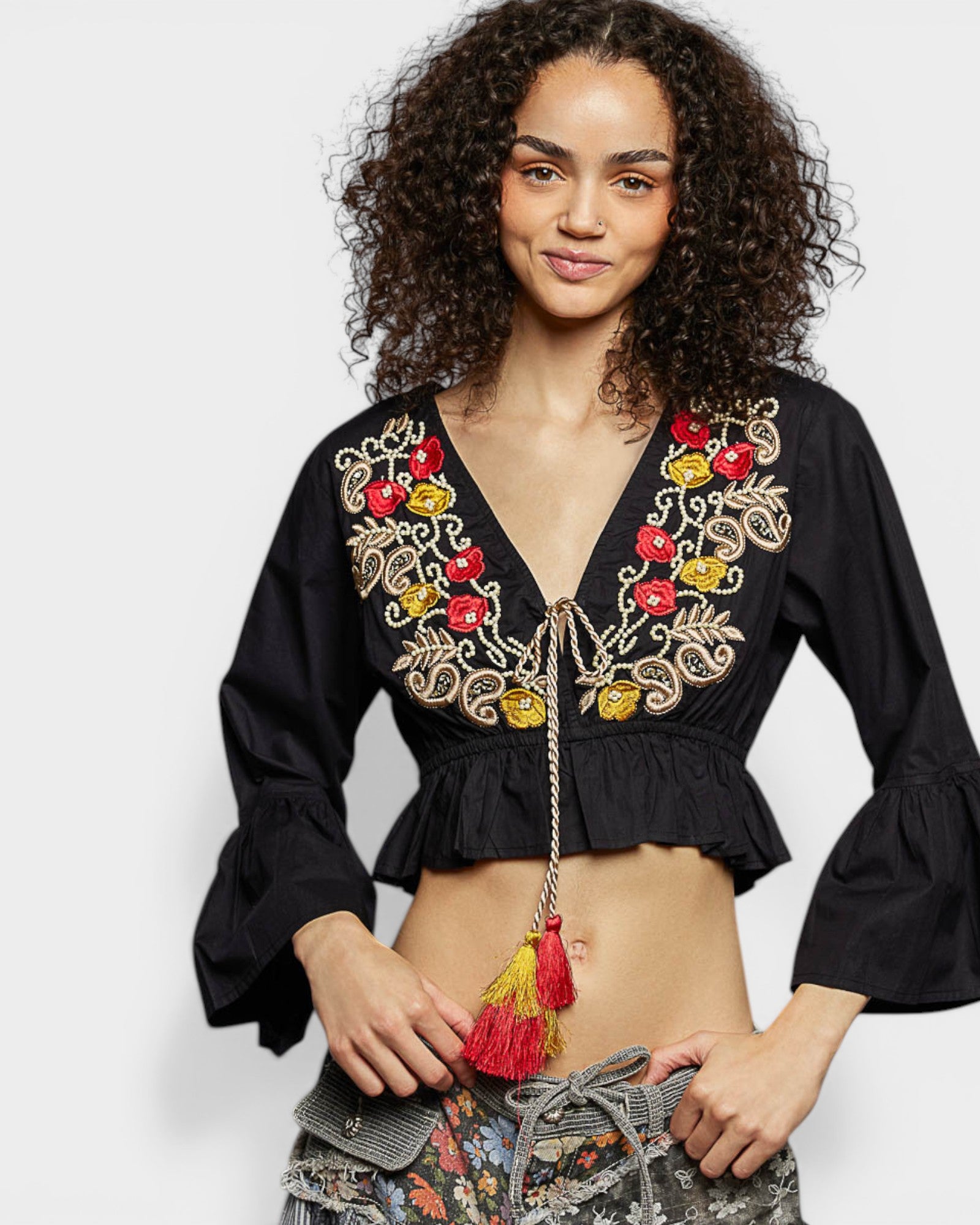 Woman wearing a black embroidered top with colorful details on a white background