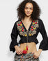Woman wearing a black embroidered top with colorful details on a white background