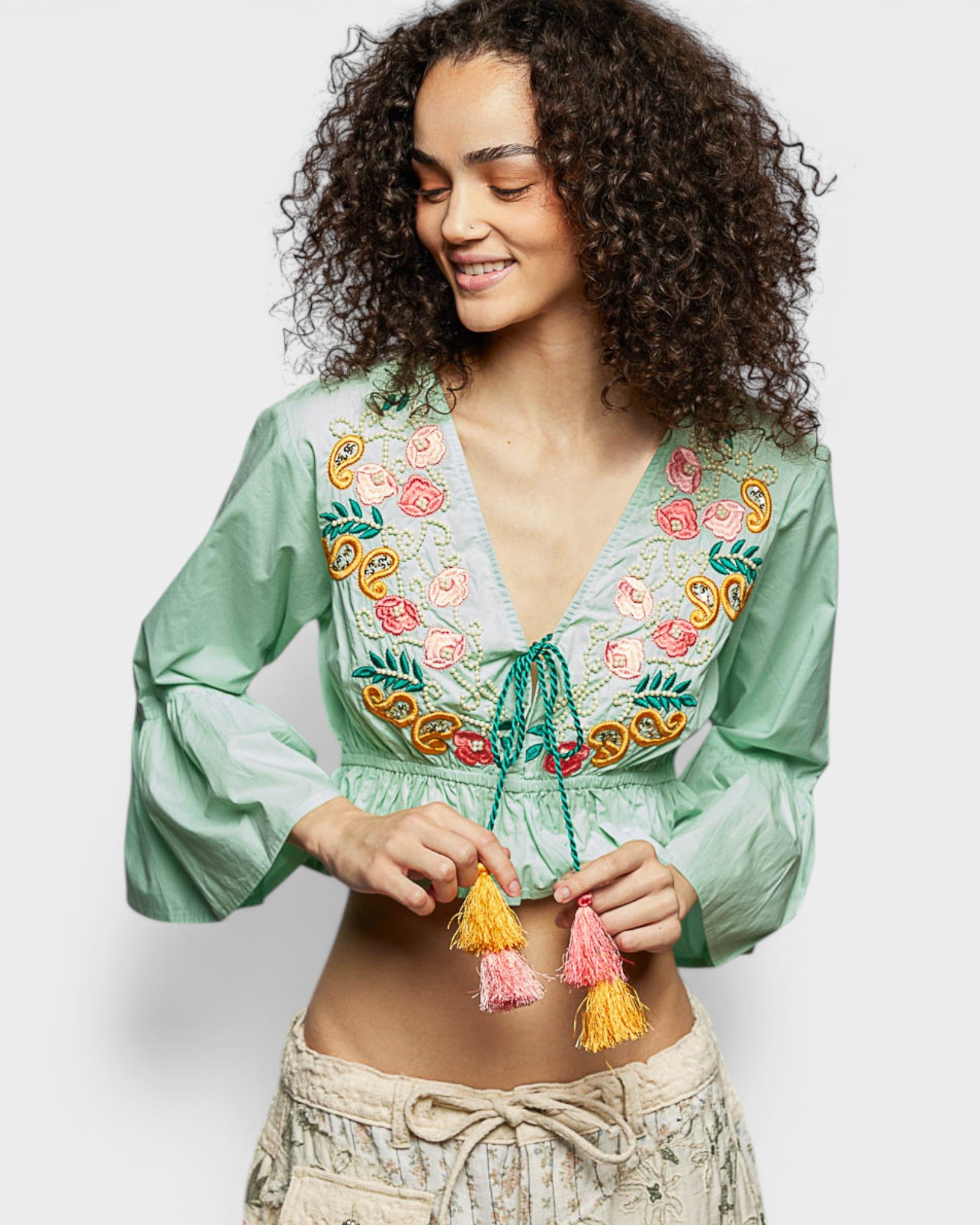 Woman wearing a green embroidered blouse with colorful tassels on a white background