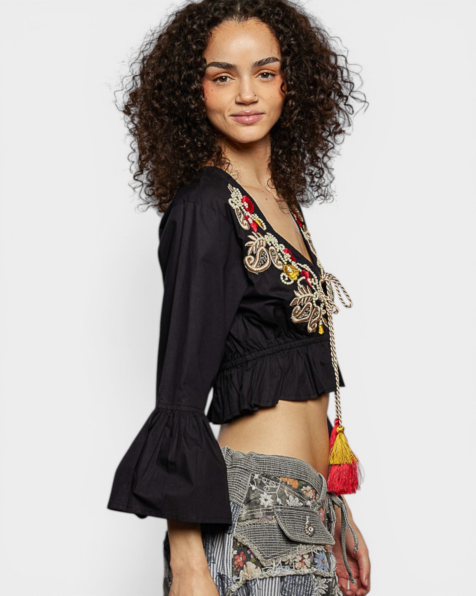 Woman wearing a black embroidered top with colorful details on a white background