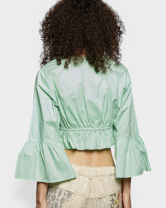 Person wearing a light green blouse with ruffled sleeves on a plain background