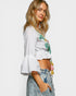 Woman wearing a white embroidered blouse with ruffled sleeves and denim shorts on a plain background
