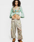 Woman wearing a green embroidered top and patterned pants on a white background