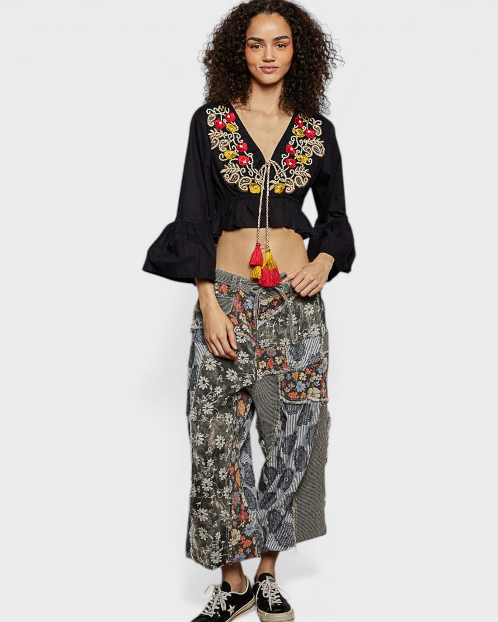 Woman wearing a black embroidered top and patterned pants on a white background