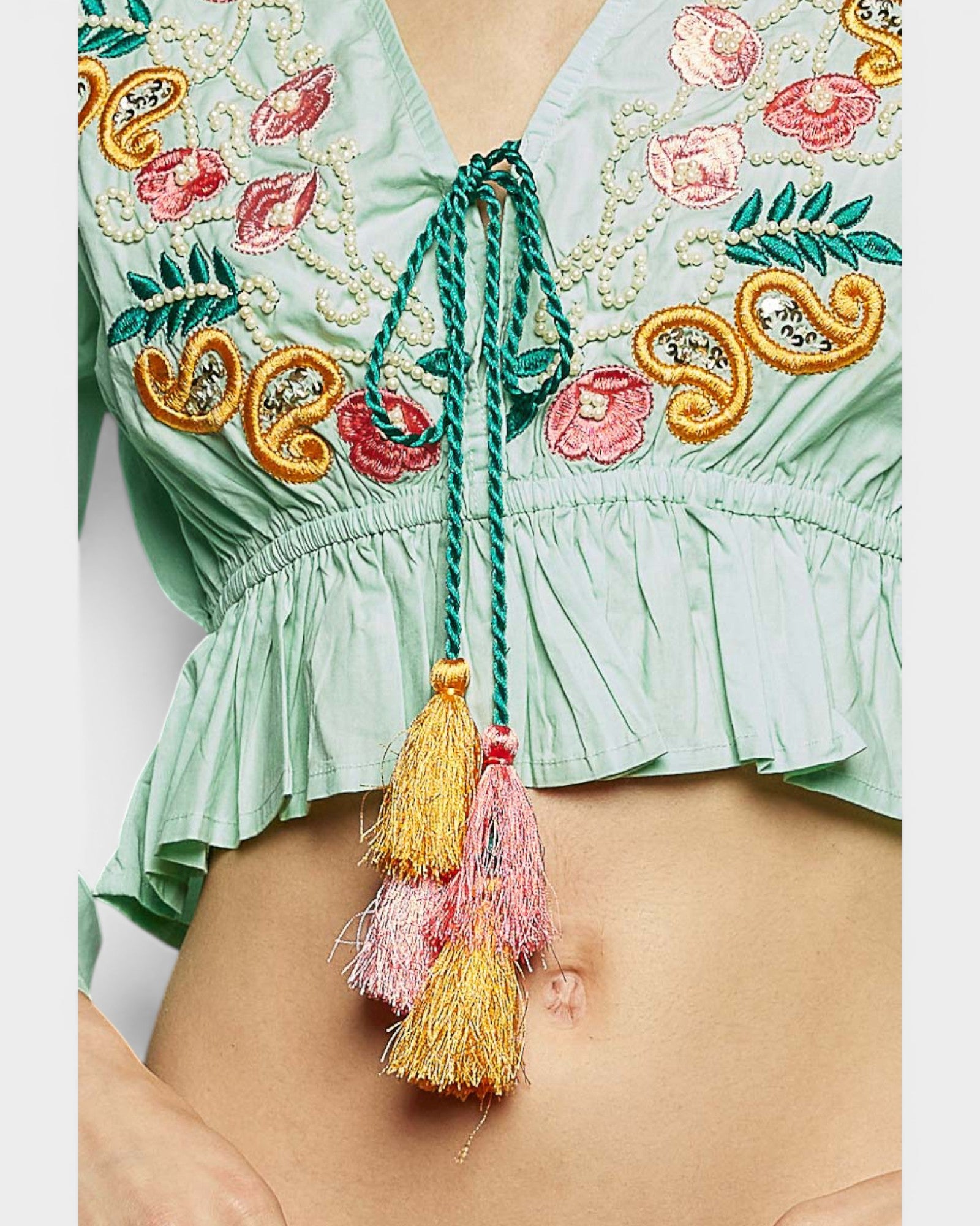 Light green embroidered top with colorful tassels on a plain background