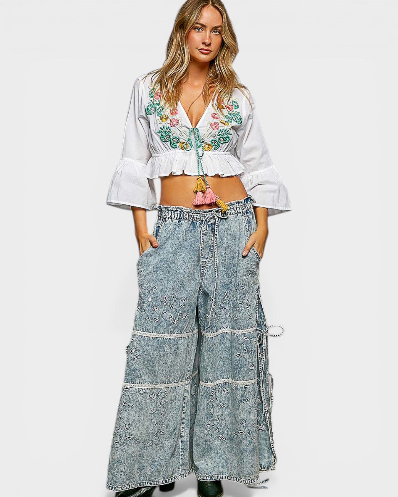 Woman wearing a white embroidered top and blue denim wide-leg pants on a white background
