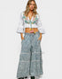 Woman wearing a white embroidered top and blue denim wide-leg pants on a white background