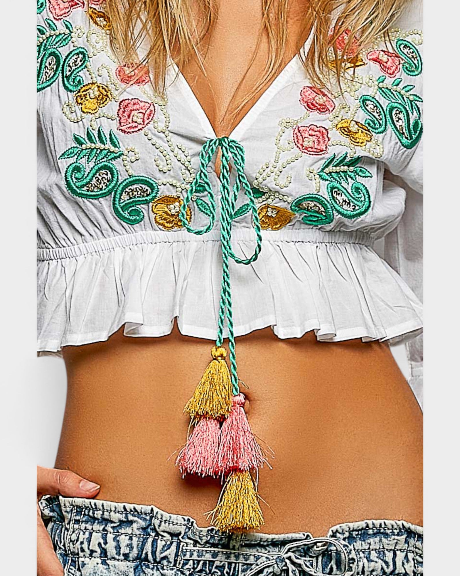 White embroidered top with colorful tassels and ruffles on a plain background