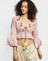 Woman wearing a pink embroidered top with ruffled sleeves on a white background