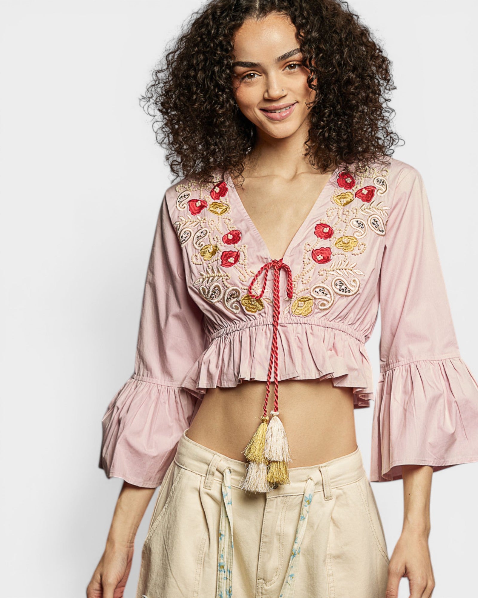 Woman wearing a pink embroidered blouse with ruffled sleeves on a white background