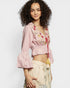 Woman wearing a pink embroidered top with ruffled sleeves on a white background