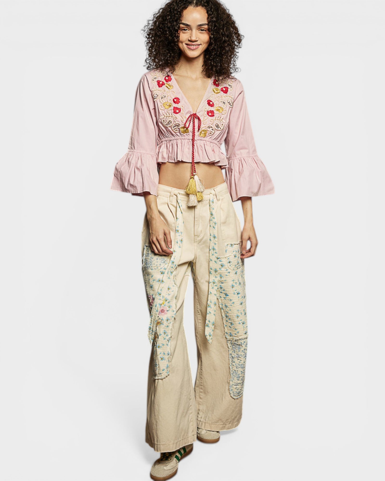 Woman wearing a pink embroidered top and beige floral pants on a white background