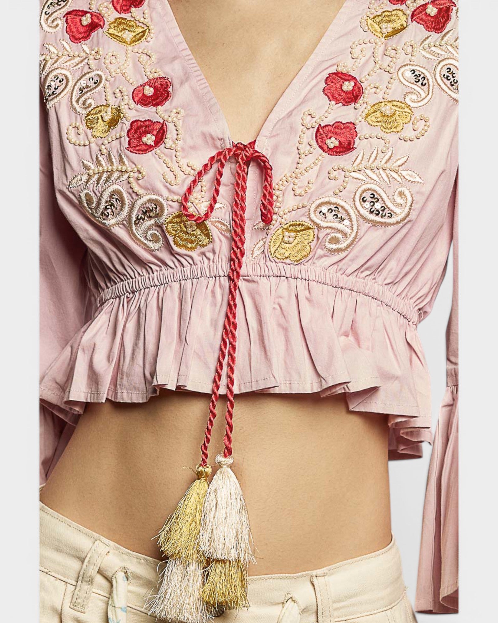 Pink embroidered top with tassels on a plain background