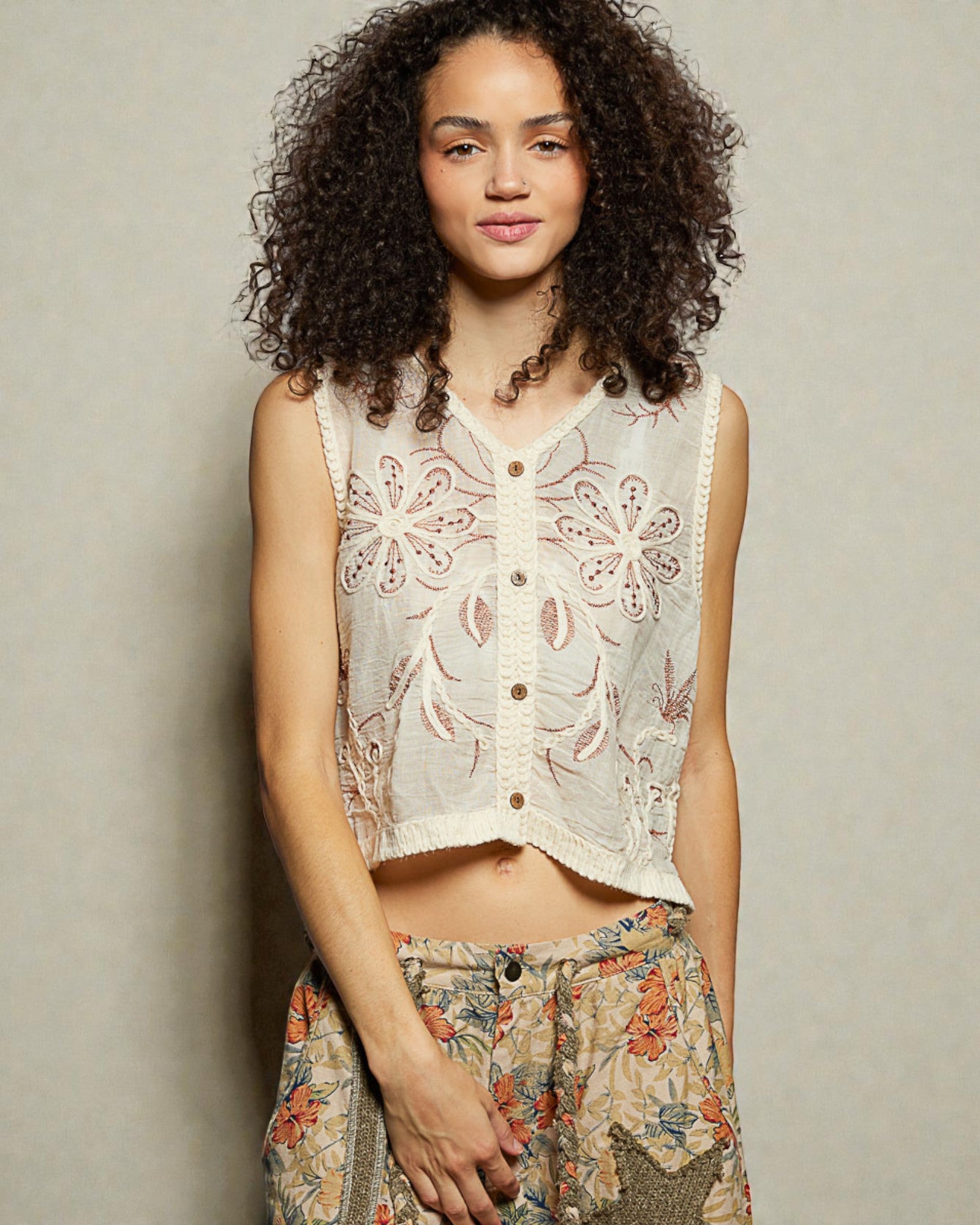 Woman wearing a floral sleeveless top and patterned pants against a neutral background