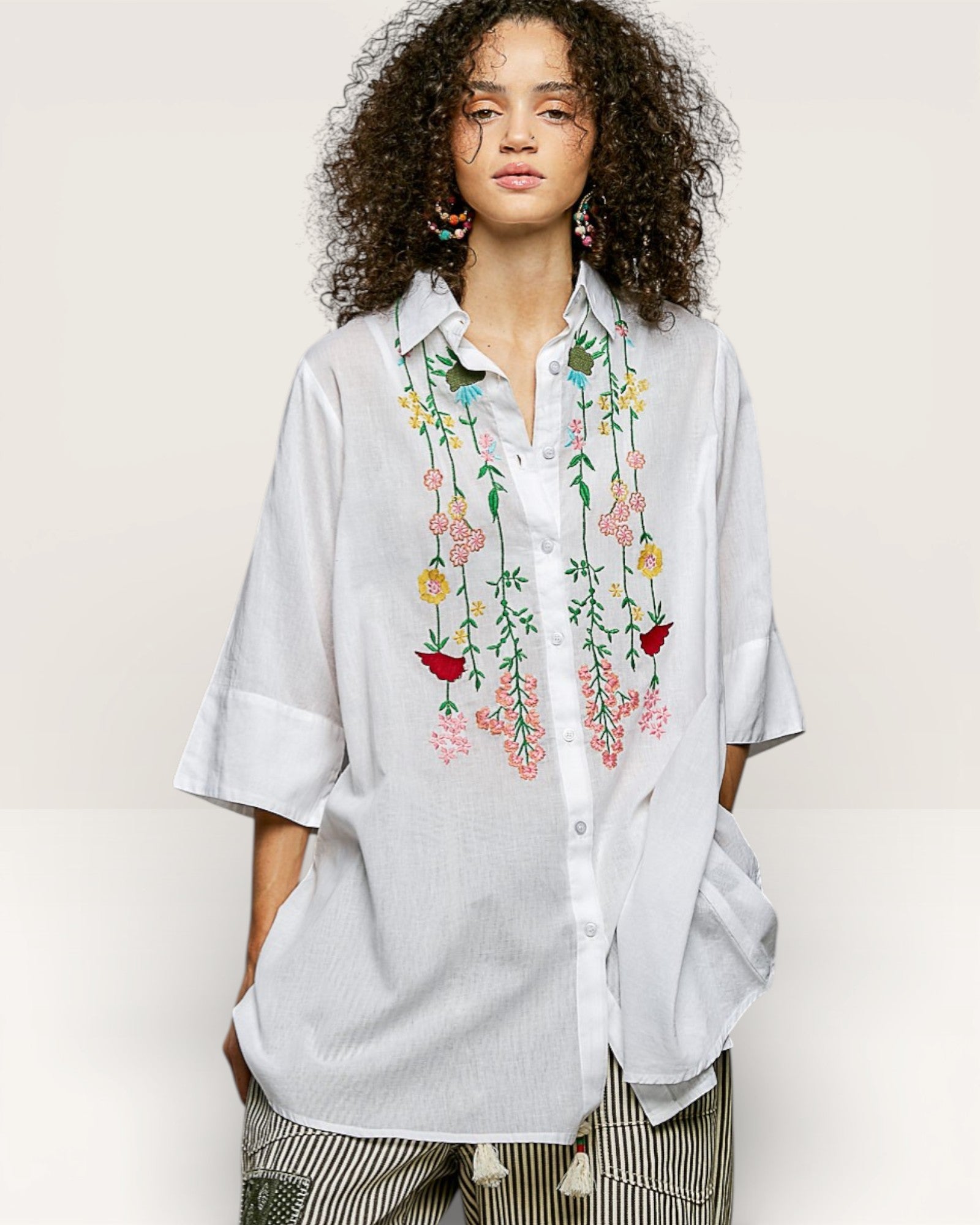 Woman wearing a light blue shirt with floral embroidery on a plain background