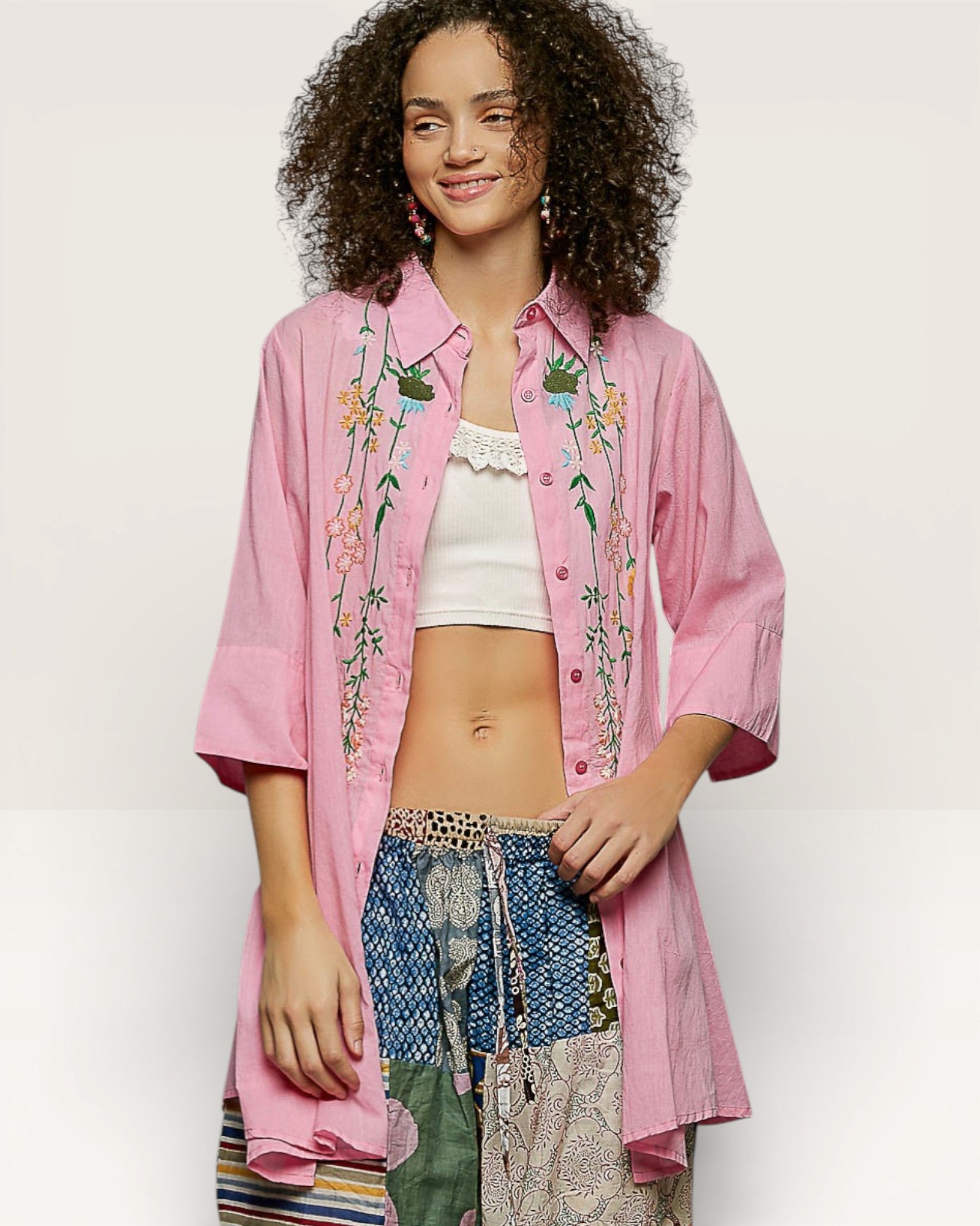 Person wearing a pink embroidered shirt with a white top and patterned pants on a plain background