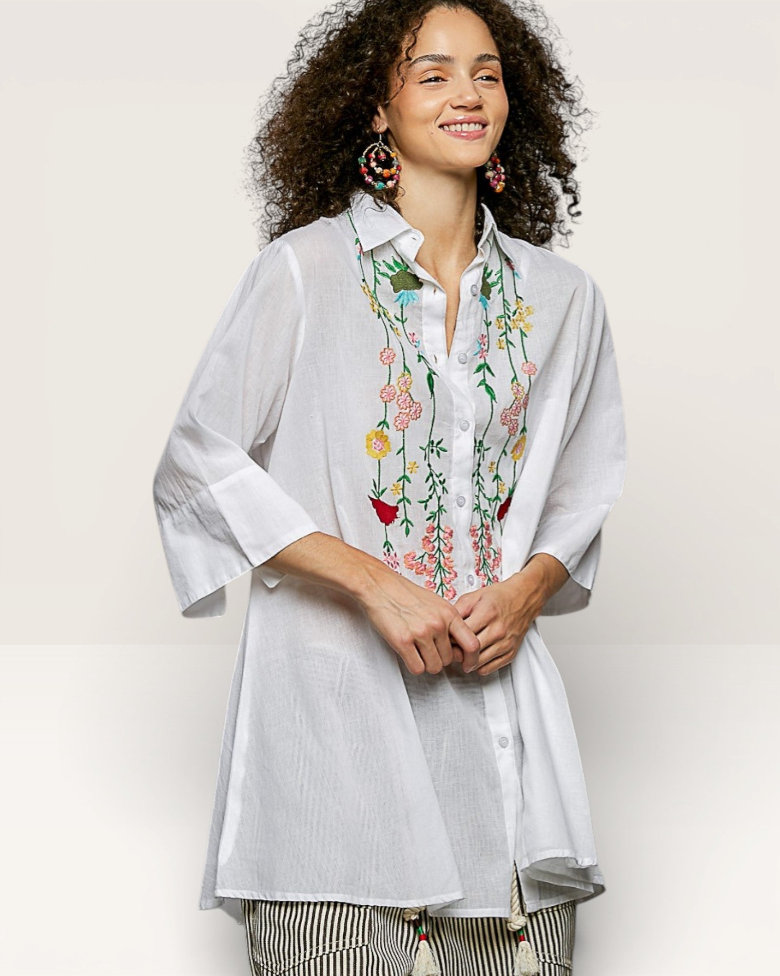 Woman wearing a light gray embroidered shirt with floral patterns on a plain background