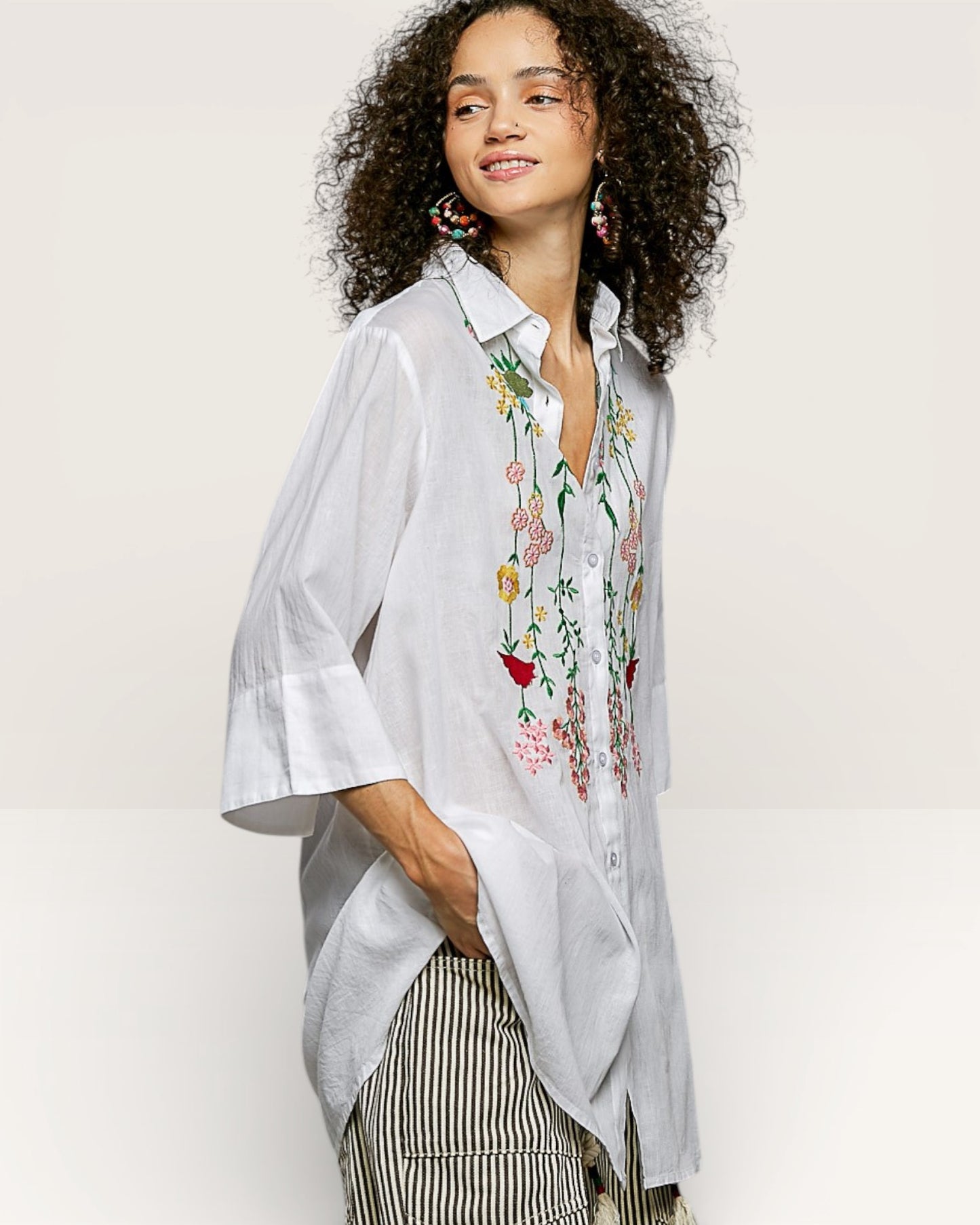Woman wearing a light gray shirt with floral embroidery on a plain background