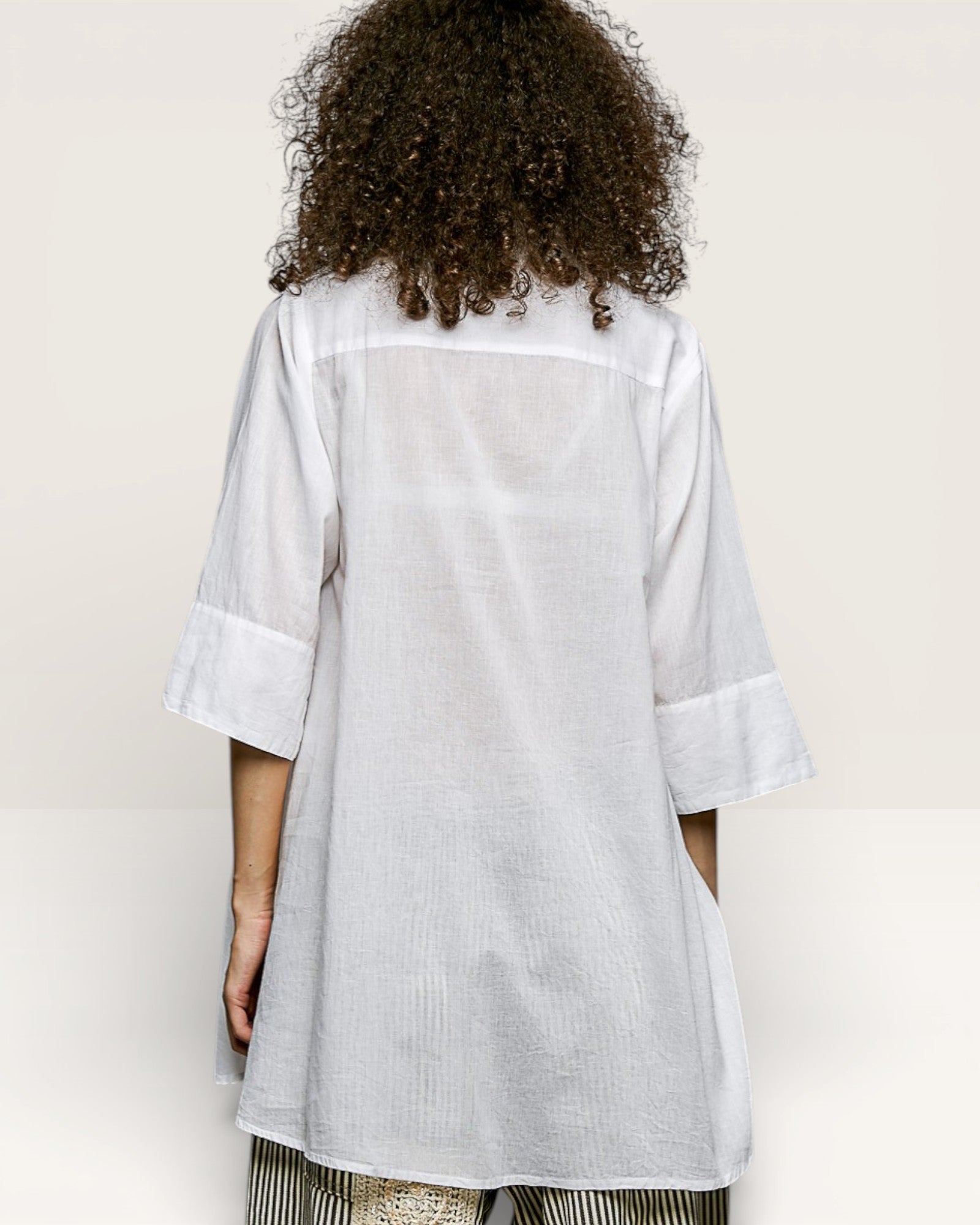 Person wearing a light gray shirt with rolled-up sleeves on a plain background