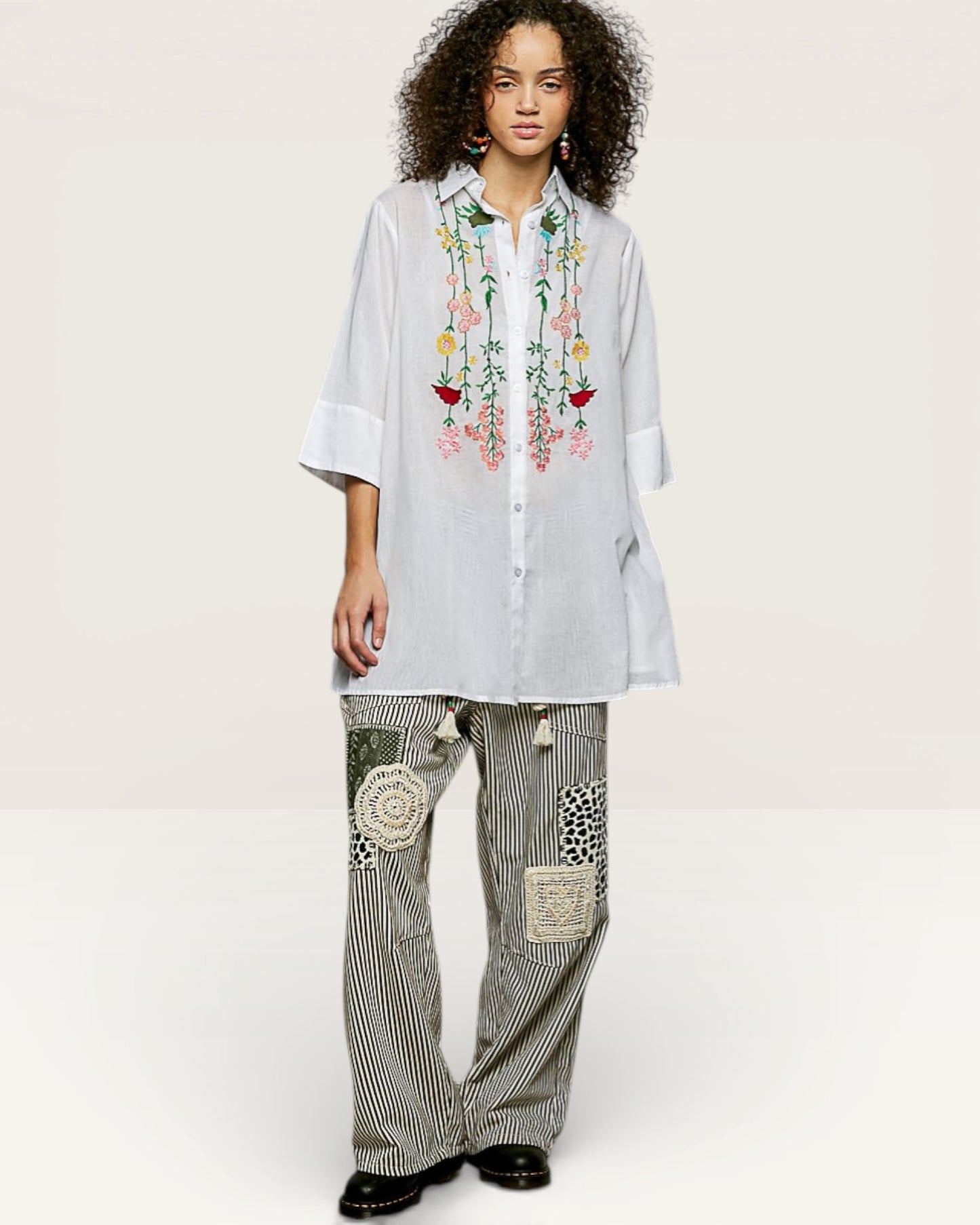 Woman wearing a light blue embroidered shirt and patterned pants on a white background