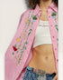Person wearing a pink embroidered shirt with floral designs, white top, and patterned pants.