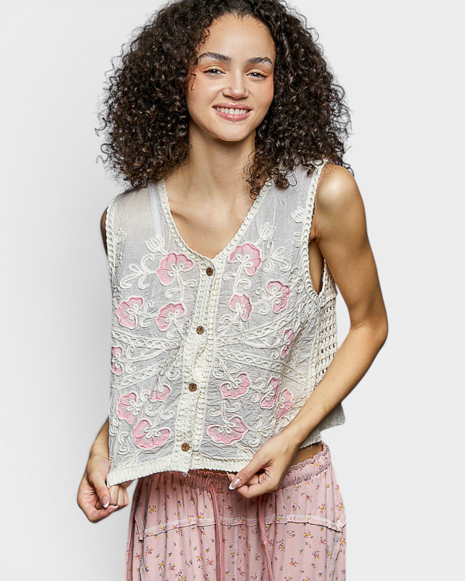 Woman wearing a floral lace vest over a pink dress on a plain background