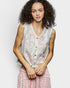 Woman wearing a sleeveless embroidered top with pink butterfly designs on a plain background