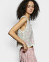 Woman wearing a sleeveless lace top with floral patterns on a plain background