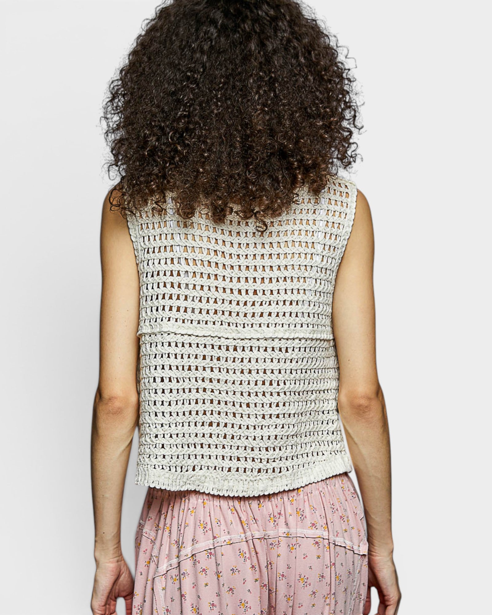 Person wearing a sleeveless crochet top with a plain background