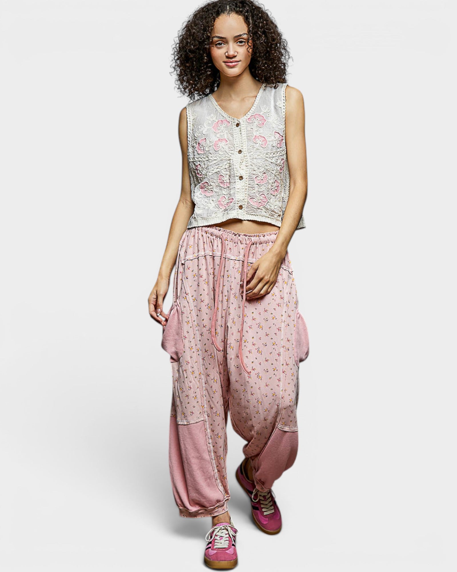 Woman wearing a sleeveless top and pink pants with floral patterns on a white background