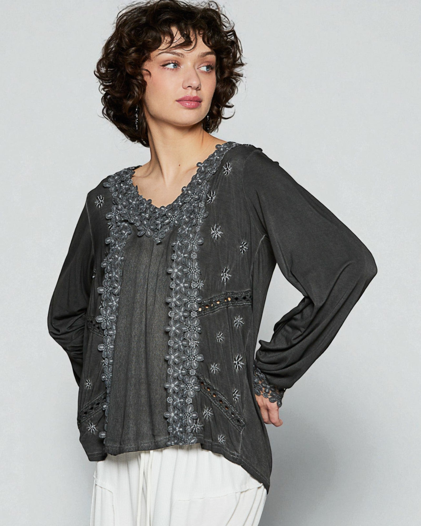 Woman wearing a dark gray blouse with floral embroidery on a light gray background