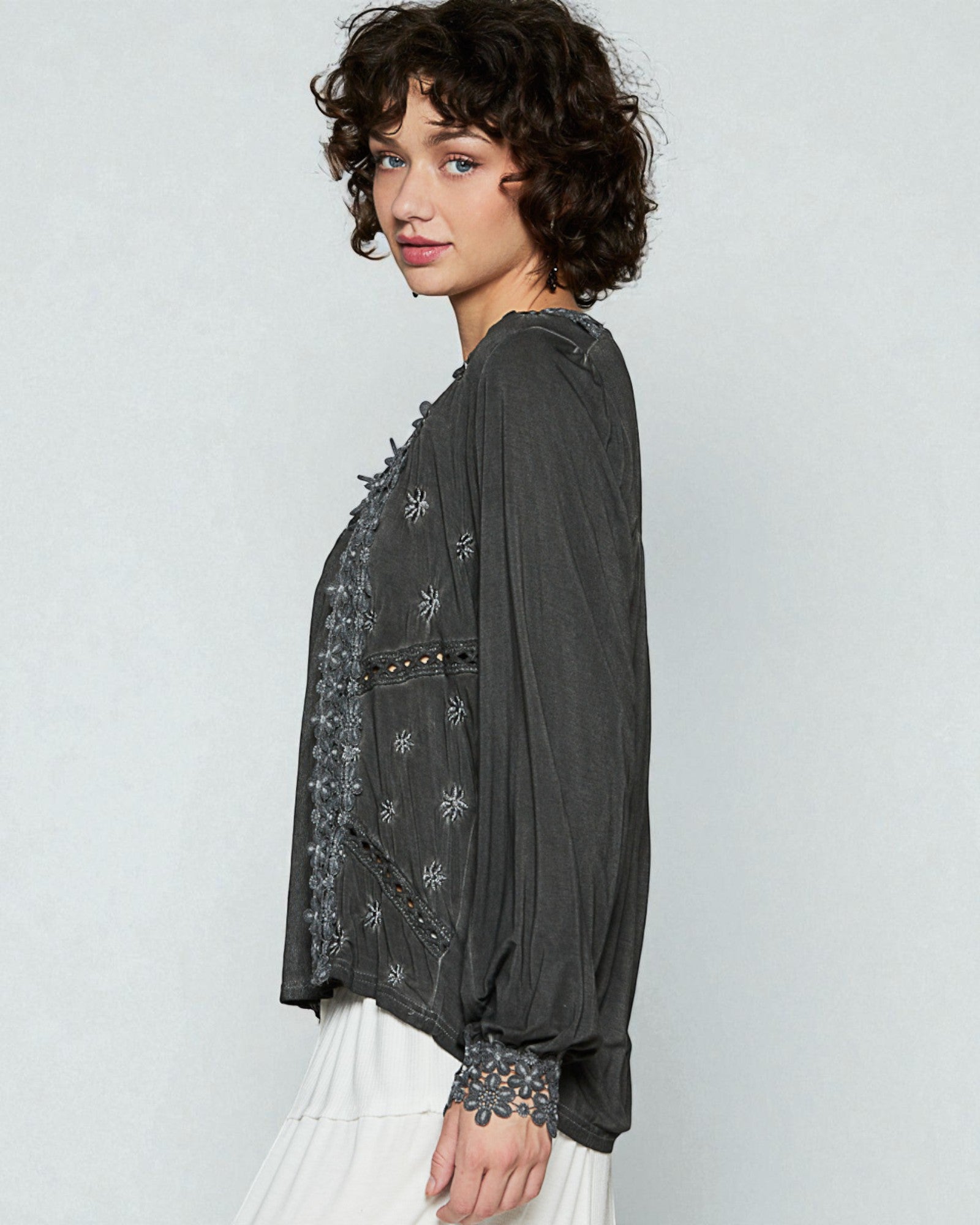 Woman wearing a dark gray embroidered blouse against a light gray background
