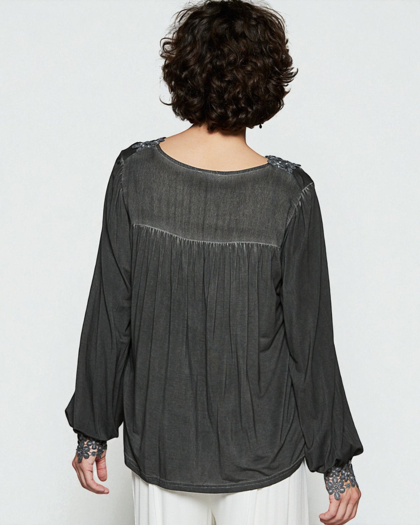 Person wearing a dark gray blouse with floral embellishments on a white background