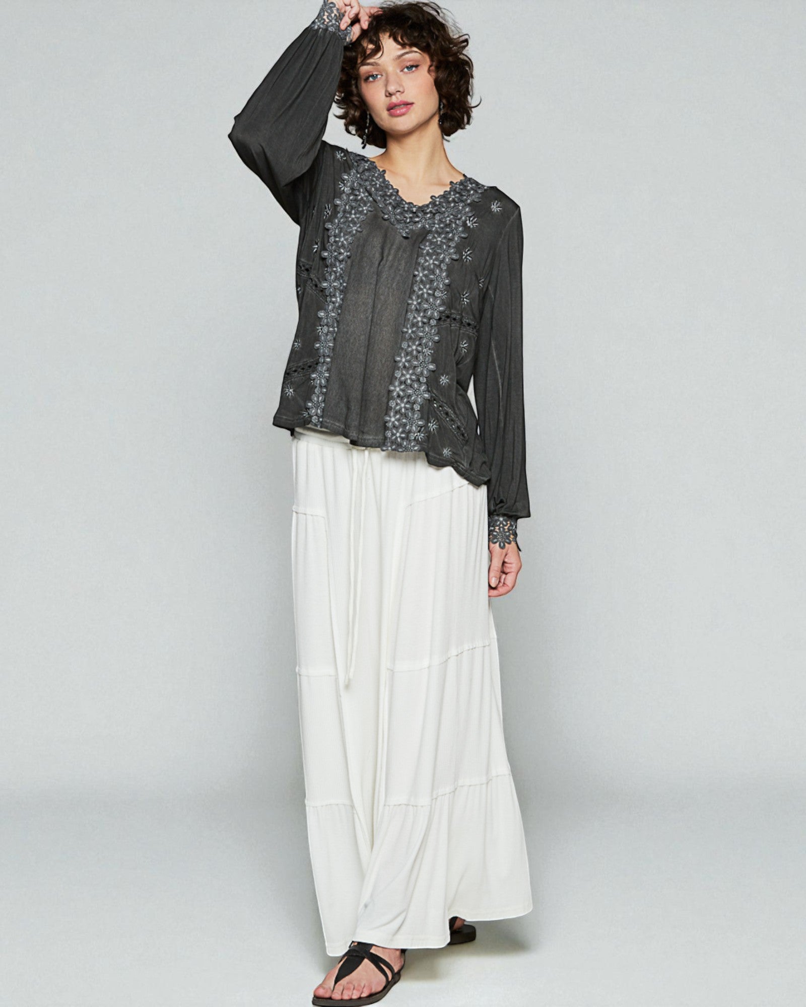 Woman wearing a black floral top and white pants on a gray background