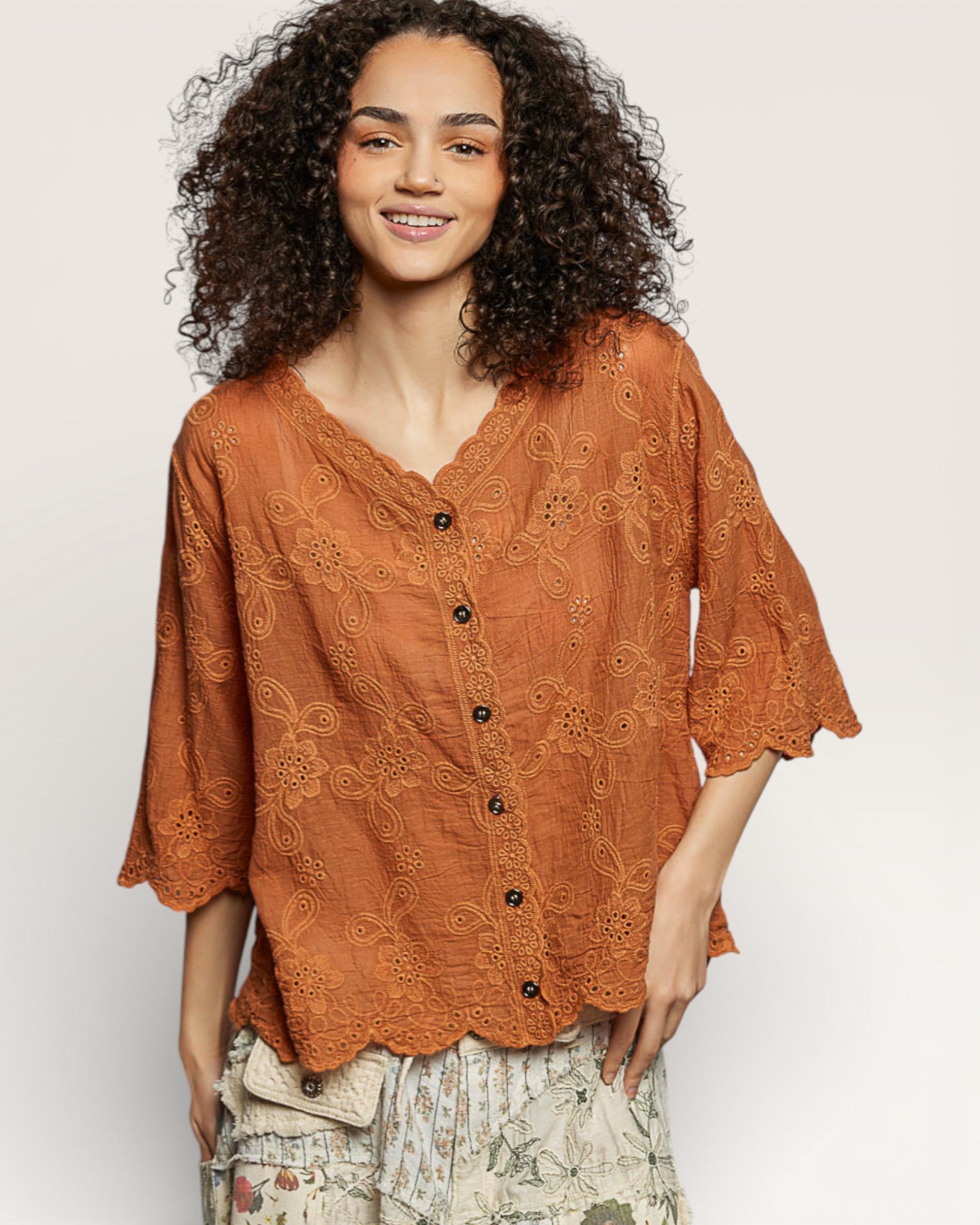 Woman wearing a rust-colored embroidered blouse against a plain background