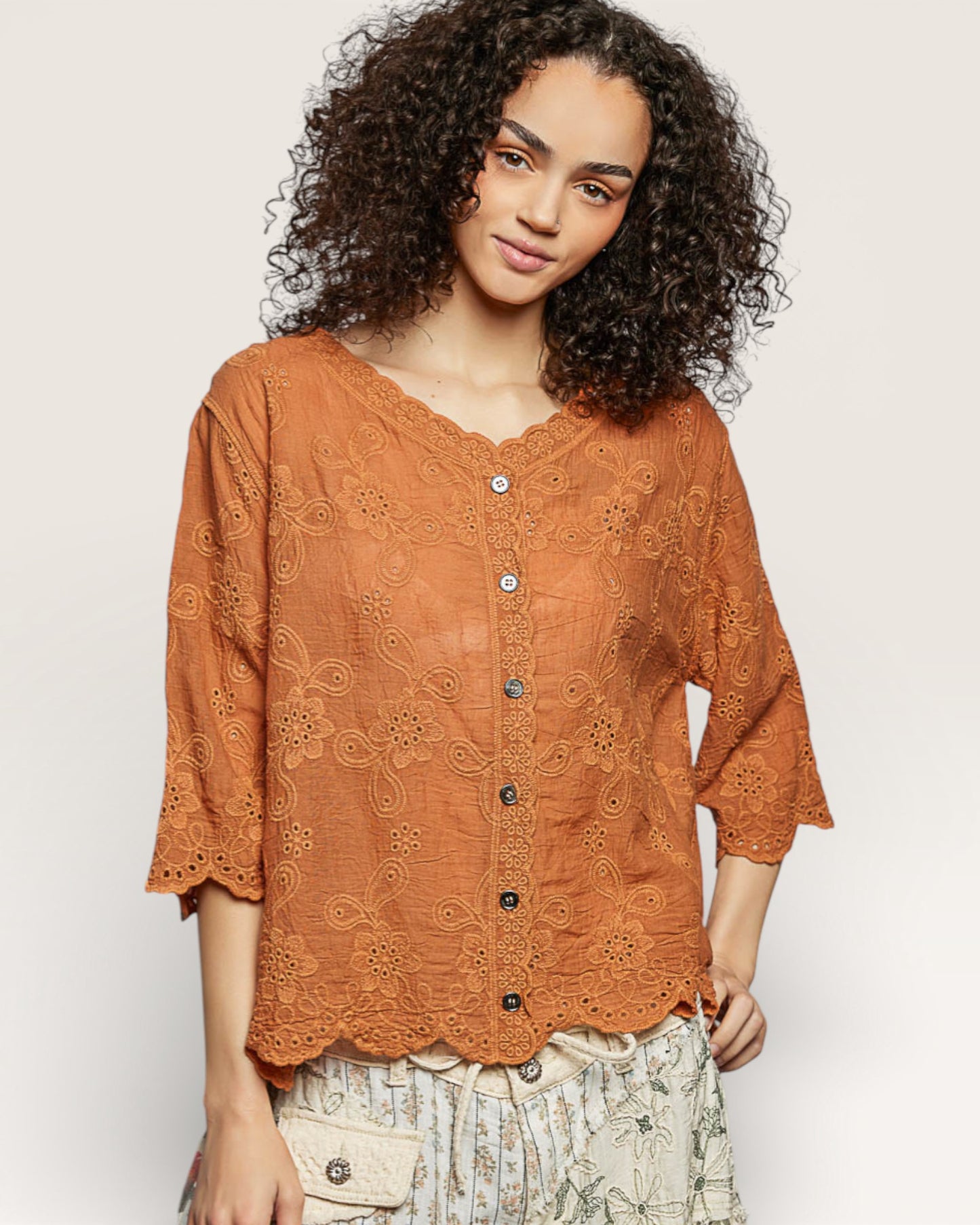 Woman wearing a rust-colored lace blouse with black buttons on a white background