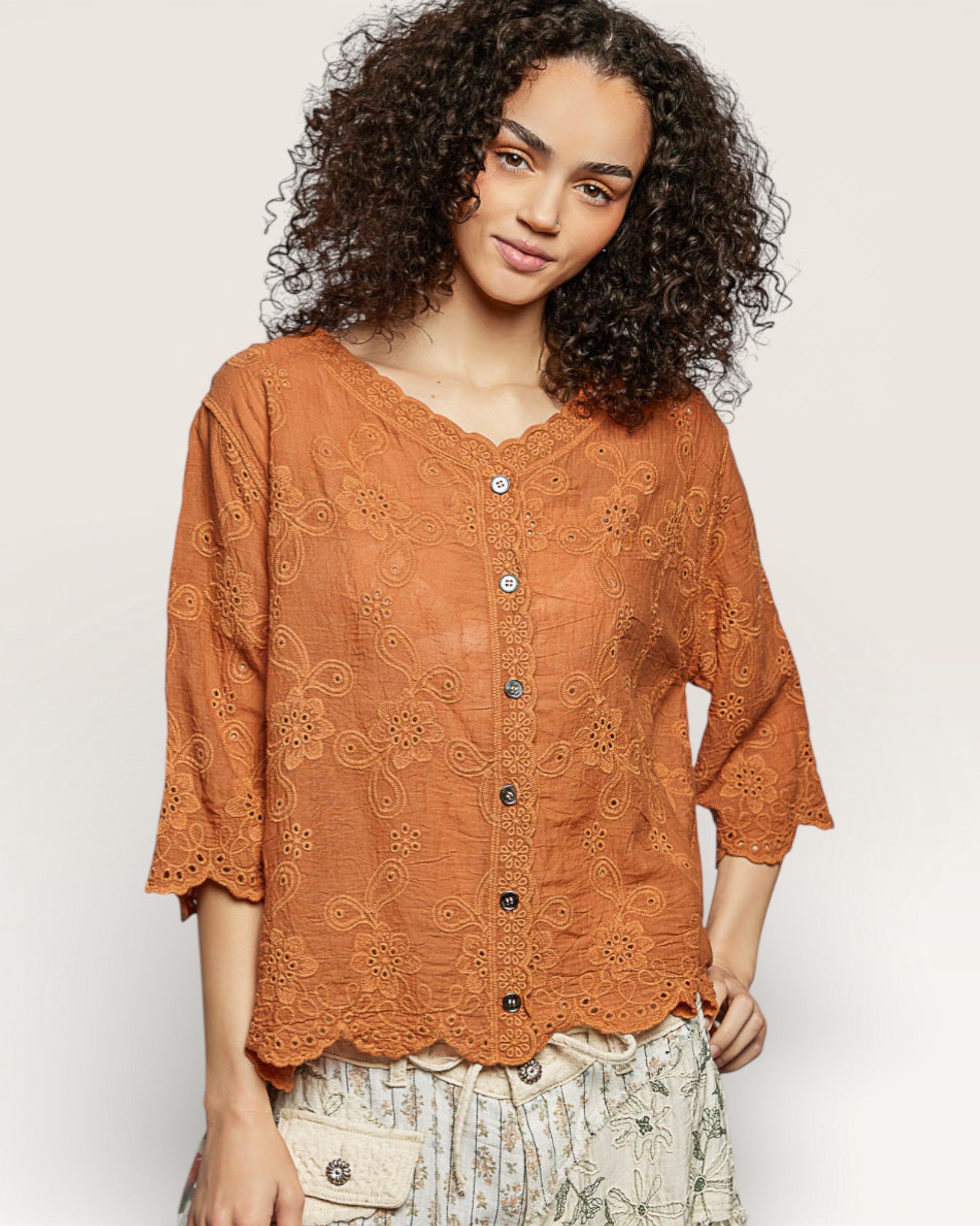 Woman wearing a rust-colored lace blouse with black buttons on a white background
